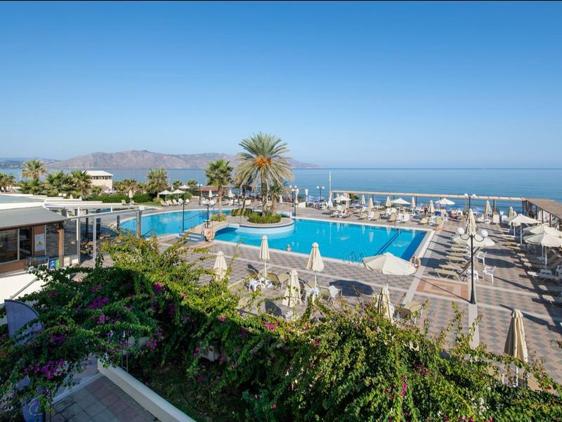 Hotelanlage mit großem Pool, Liegestühlen, Palmen und Meerblick unter klarem Himmel.
