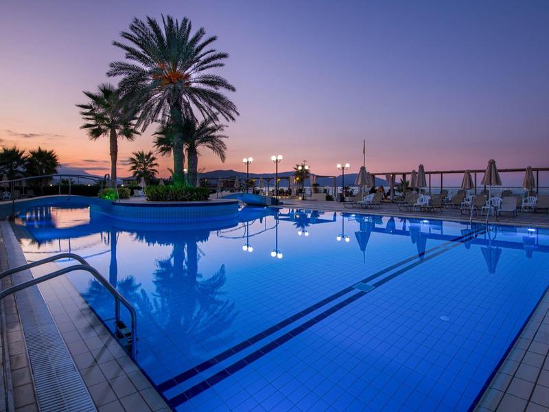 Abendstimmung am Pool mit blauem Wasser, Palmen und Sitzbereichen bei Sonnenuntergang.