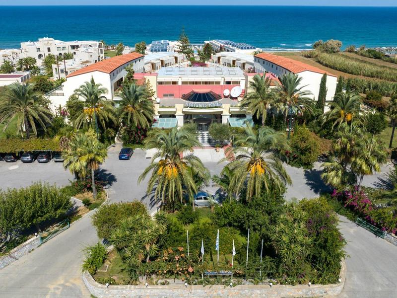 Große Hotelanlage mit roten Dächern, türkisfarbenem Meer im Hintergrund und vielen Palmen im Vordergrund.