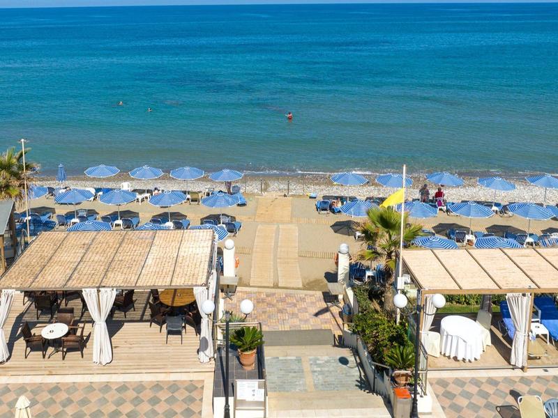 Blick auf einen Strand mit Sonnenschirmen, Liegen und Holzstegen am blauen Meer.