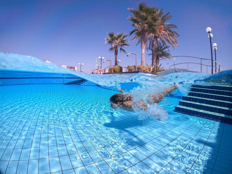 Ein Schwimmer taucht im klaren blauen Wasser eines Pools mit Palmen und blauem Himmel.