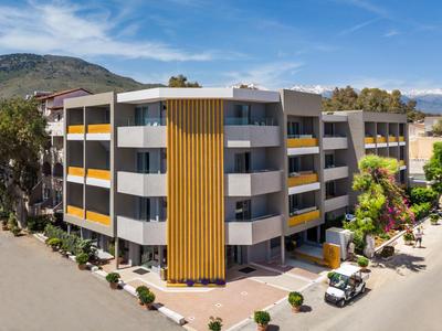 Nowoczesny budynek hotelu z żółtymi akcentami, otoczony zielenią i widokiem na góry.