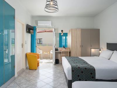 Jasny pokój hotelowy z dwoma łóżkami, żółtym fotelem, szafą i drzwiami na balkon.