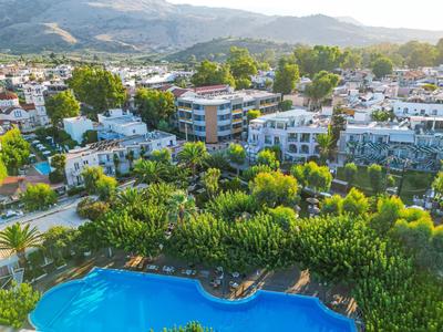 Blick auf Stadt mit weißen Gebäuden, viel Grün und klarem blauen Schwimmbecken im Vordergrund.