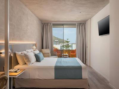 Nowoczesny pokój hotelowy z podwójnym łóżkiem, balkonem i telewizorem na ścianie.