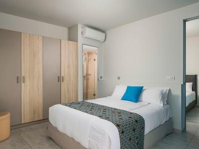 Prosty pokój hotelowy z łóżkiem podwójnym, białą pościelą, niebieską poduszką, drewnianą szafą i klimatyzacją.