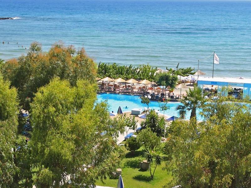 Nadmorski ośrodek z basenami, zielenią i skalistą plażą z czystą, niebieską wodą.