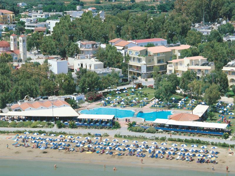 Kurort nadmorski z parasolami, basenami, zielenią i budynkami za brzegiem.