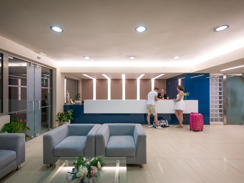 Recepcja hotelowa z nowoczesnymi sofami, ladą recepcyjną i gośćmi meldającymi się z bagażem.