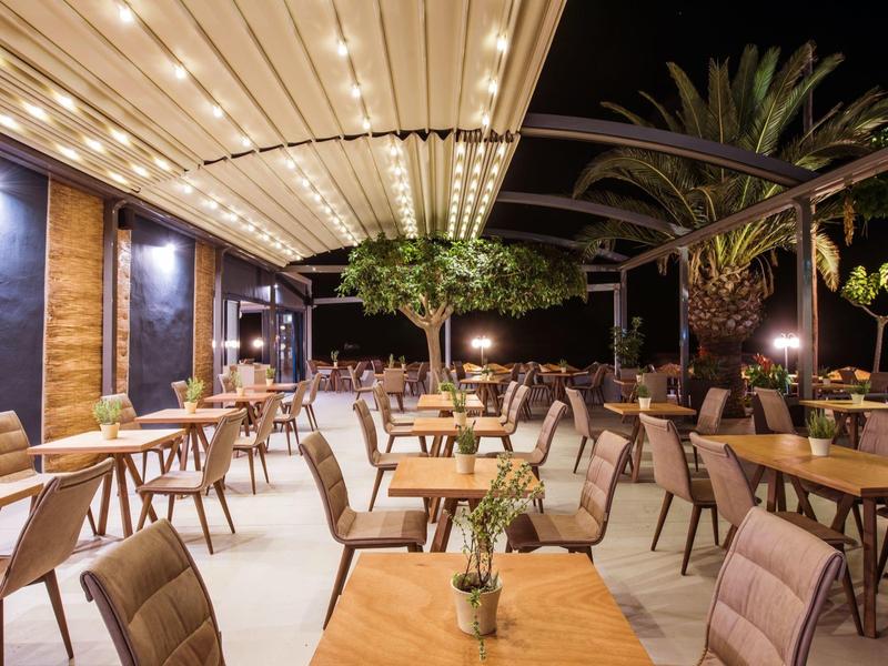 Zewnętrzna część restauracji hotelowej z drewnianymi stołami i krzesłami pod jasnym oświetleniem nocą.