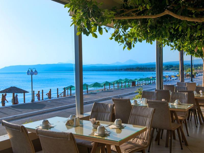 Strefa jadalna na zewnątrz z widokiem na spokojne morze i parasole plażowe pod czystym niebem.