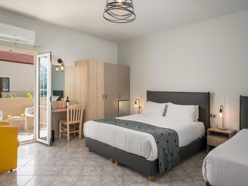 Nowoczesny pokój hotelowy z podwójnym łóżkiem, biurkiem, szafą, otwartymi drzwiami na balkon i podłogą z płytek.