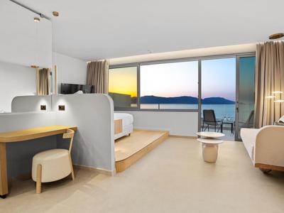 Modernes Hotelzimmer mit großem Fenster, Ausblick auf Meer, hellen Möbeln und hellem Teppichboden.