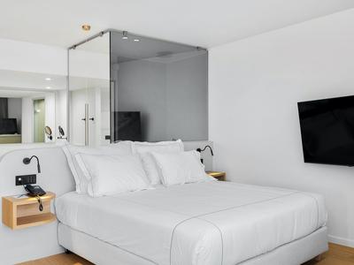 Weißes Schlafzimmer mit großem Bett, Wand-TV und minimalistischen Holznachtischen.