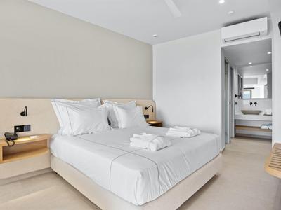 Modernes Schlafzimmer mit Doppelbett, weißen Wänden, eingebauten Nachttischen und Zugang zu Badezimmer.