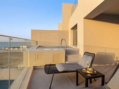 Balkon mit gelben Wänden, Glasgeländer, Whirlpool, zwei schwarzen Stühlen und kleinem Tisch mit Obst.