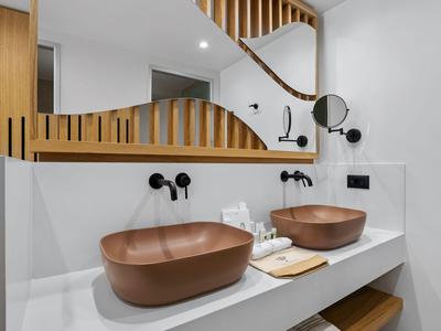 Área de baño moderna con dos lavabos marrones, encimera blanca y espejo grande.