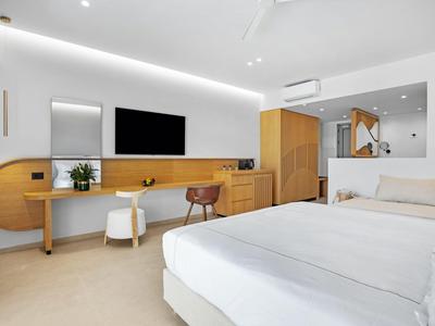 Habitación de hotel moderna con una cama grande, muebles de madera clara y un televisor montado en la pared.