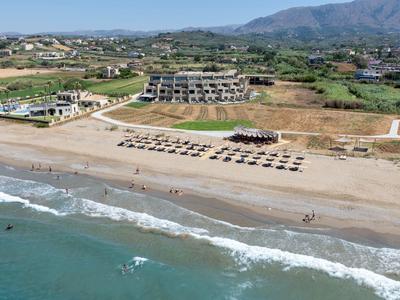 Strand mit Sonnenschirmen, Gebäuden am Ufer und Bergen im Hintergrund unter klarem Himmel.