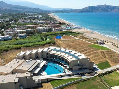 Complejo hotelero moderno con piscina junto a la playa, rodeado de montañas y mar.