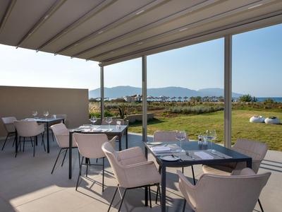 Terraza cubierta con mesas puestas con vistas a un césped verde y montañas.