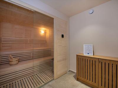 Sala de sauna con bancos de madera, cubo de madera, iluminación interior y calentador moderno.