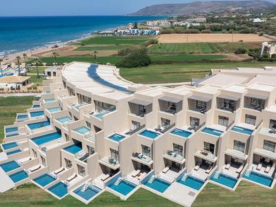 Complejo hotelero moderno con piscinas privadas cerca de una larga playa de arena y colinas de fondo.