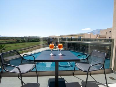 Balcón con dos sillas y mesa, con vista a la piscina y paisaje.