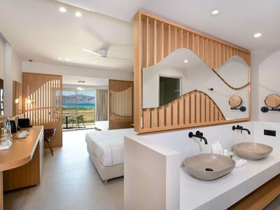 Habitación de hotel moderna con cama doble, baño con dos lavabos y balcón con vista al mar.