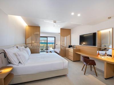 Habitación de hotel luminosa con cama doble, escritorio, televisor y vista a la costa.