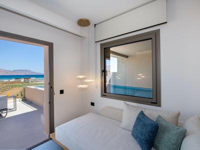 Habitación de hotel luminosa con terraza, vista al mar y asiento cómodo con cojines.