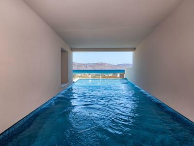 Piscina cubierta moderna con vistas a montañas y mar, agua clara y arquitectura minimalista.