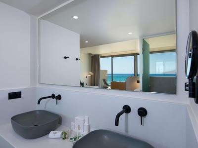 Baño de hotel moderno con dos lavamanos, espejo grande y vista al mar.