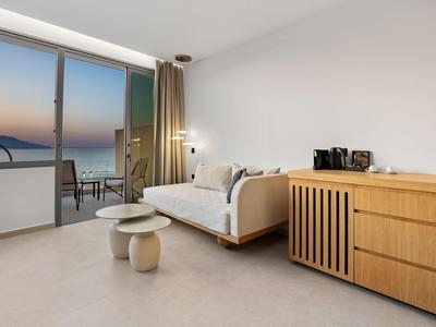 Habitación de hotel moderna con vista al mar, sofá, mesas auxiliares y cómoda.