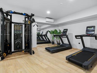 Modern gym with treadmills, workout machine, and mirrored wall on light wood floor.