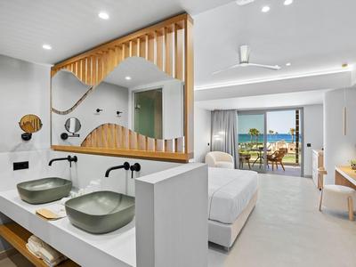 Modern hotel room with double bed, two sinks, and view of terrace and sea.