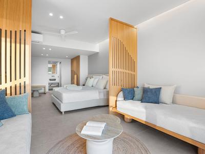 Modernes Schlafzimmer mit weißen Wänden, Holzakzenten, zwei Betten und blau-grauen Kissen.