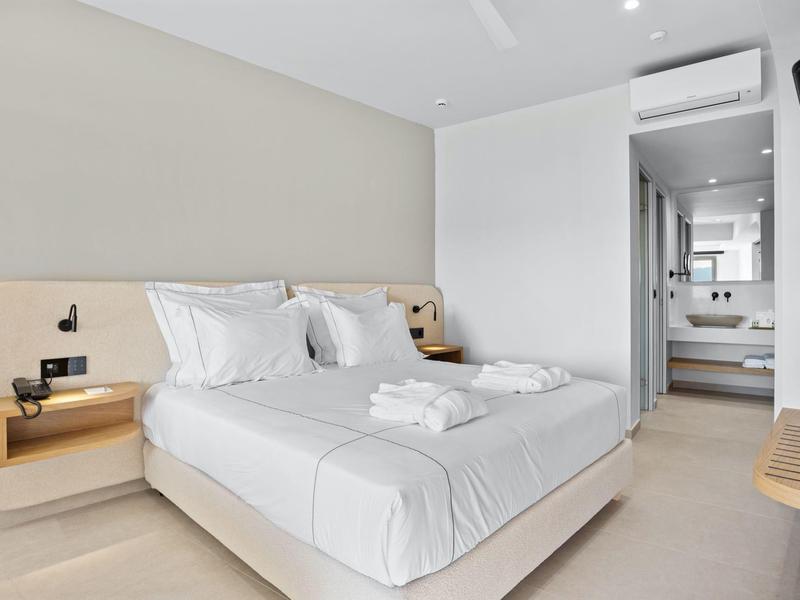 Modernes Schlafzimmer mit Doppelbett, weißen Wänden, eingebauten Nachttischen und Zugang zu Badezimmer.