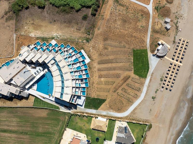 Luftaufnahme von halbkreisförmigen blauen Sonnenschirmen neben einem Gebäude am Sandstrand mit Meer.