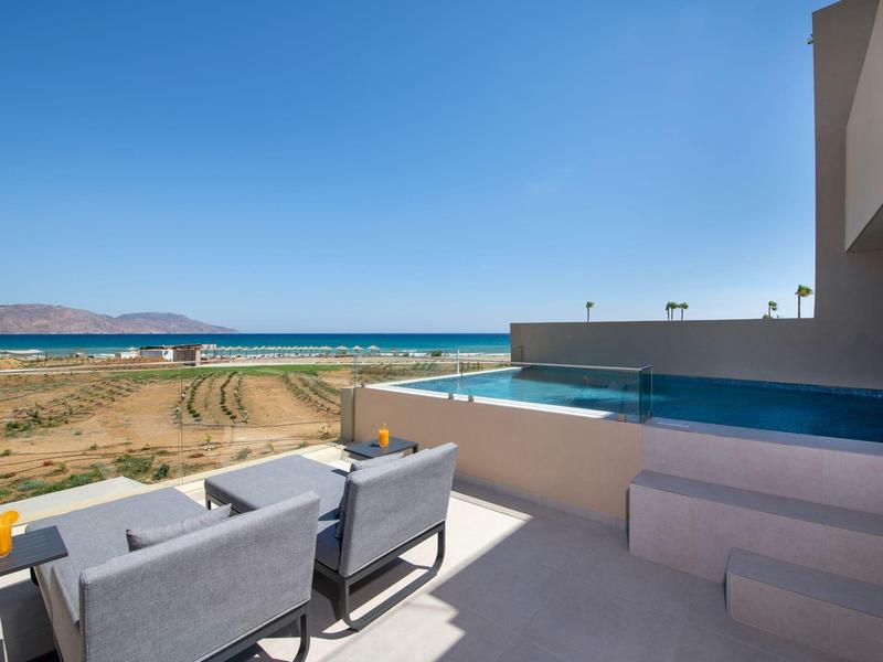 Terrasse mit grauen Sitzmöbeln, Glasrelief und Meerblick unter klarem blauem Himmel.