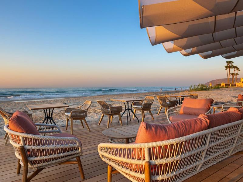Strandterrasse mit Korbsesseln, Tischen und Blick auf das Meer bei Sonnenuntergang.