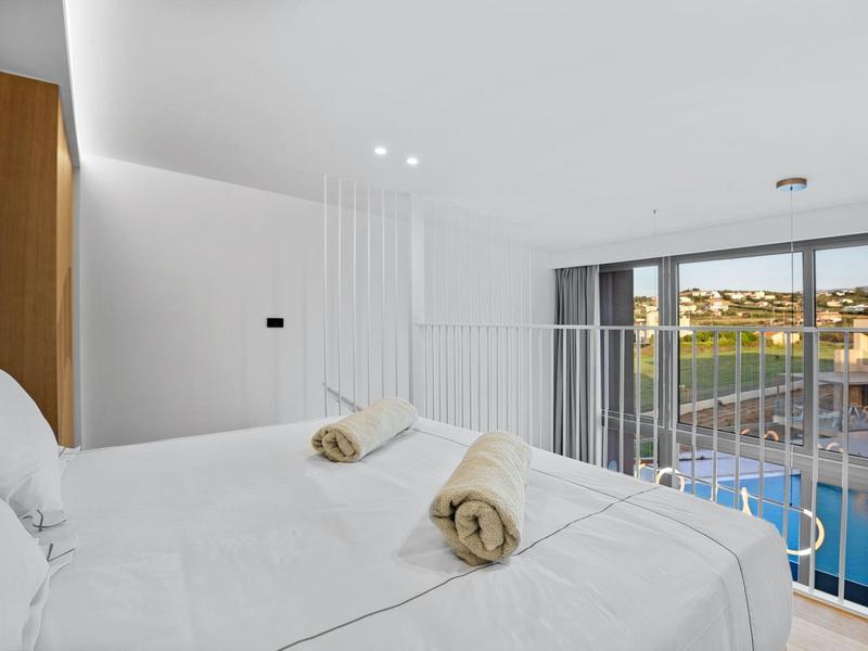 Helles Schlafzimmer mit weißer Bettwäsche, zwei eingerollten Handtüchern und Balkon mit Poolblick.