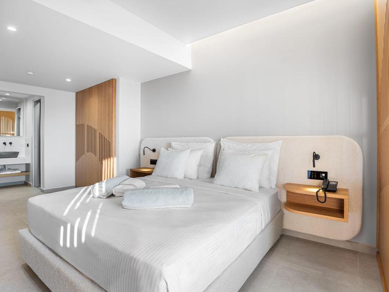 Helles Schlafzimmer mit großem Bett, weißen Wänden, integriertem Wandregal und begehbarem Kleiderschrank.