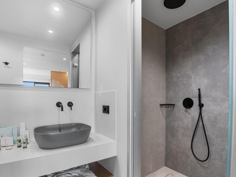 Modernes Badezimmer mit grauer Aufsatzwaschschale, schwarzem Duschkopf und hellgraßen Fliesen.