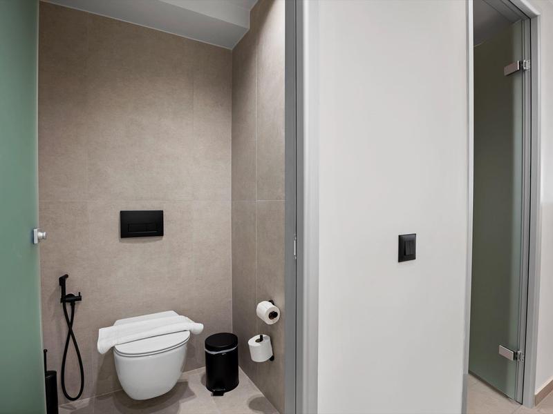 Kleines modernes Bad mit Wand-WC, Bidet-Dusche, schwarzem Mülleimer und weißem Toilettenpapierhalter.