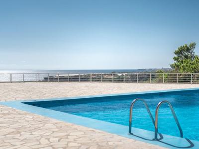 Piscina limpida con vista mare sotto un cielo azzurro e terrazza in pietra.
