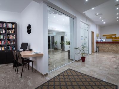 Recepción de hotel moderna con mostrador, escritorio con computadora y estantería cerca de la entrada.