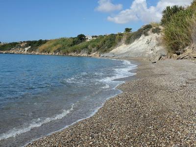 Spiaggia di ciottoli con onde leggere e scogliere vegetate sullo sfondo