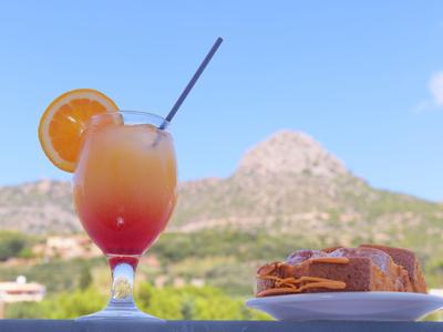 Cocktail met sinaasappelschijf naast een bord met taart voor berglandschap.