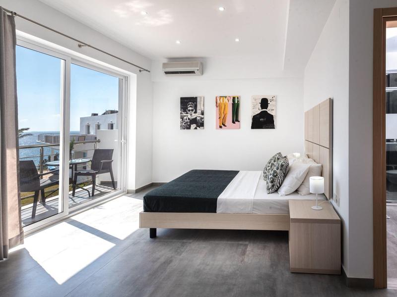 Habitación de hotel moderna con cama grande, balcón con vistas al mar y decoración minimalista.